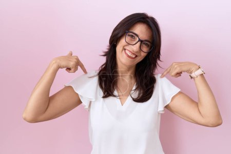 Photo for Middle age hispanic woman wearing casual white t shirt and glasses looking confident with smile on face, pointing oneself with fingers proud and happy. - Royalty Free Image
