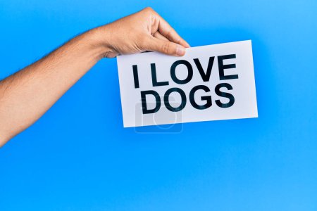 Foto de Hand of caucasian man holding paper with i love dogs message over isolated blue background - Imagen libre de derechos