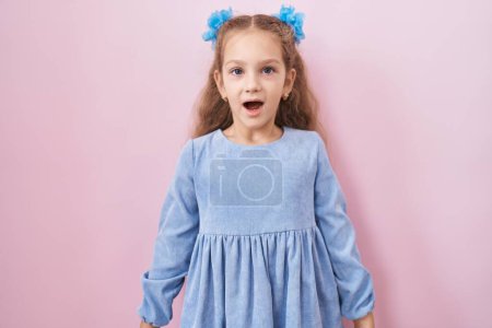 Foto de Joven niña de pie sobre el fondo rosa asustada y sorprendida con la boca abierta para sorpresa, cara de incredulidad - Imagen libre de derechos