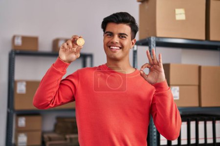 Photo for Hispanic man working at small business ecommerce holding bitcoin doing ok sign with fingers, smiling friendly gesturing excellent symbol - Royalty Free Image