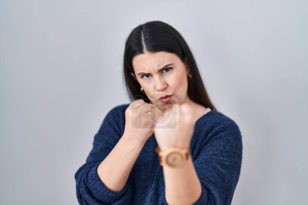 Photo for Young brunette woman standing over isolated background ready to fight with fist defense gesture, angry and upset face, afraid of problem - Royalty Free Image
