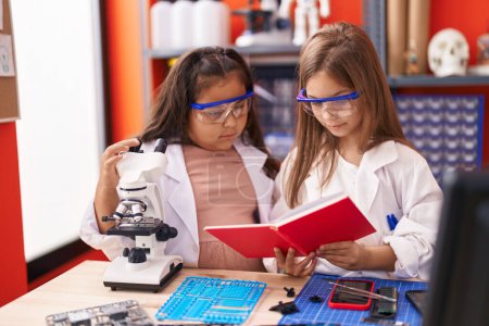 Photo for Two kids students using microscope reading notebook at laboratory classroom - Royalty Free Image