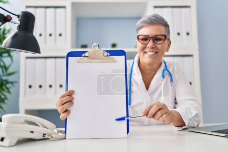 Photo for Middle age woman wearing doctor uniform holding clipboard at clinic - Royalty Free Image