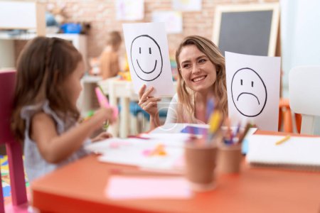 Téléchargez les photos : Enseignant et tout-petit assis sur la table ayant une thérapie émotionnelle à la maternelle - en image libre de droit