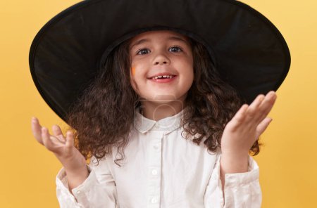 Téléchargez les photos : Adorable fille hispanique souriant en costume d'Halloween sur fond jaune isolé - en image libre de droit