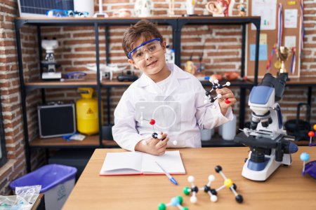 Téléchargez les photos : Adorable garçon hispanique étudiant souriant confiant tenant des molécules en classe de laboratoire - en image libre de droit