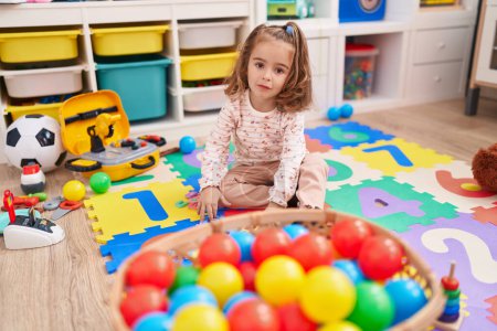 Photo for Adorable hispanic girl playing with balls sitting on floor at kindergarten - Royalty Free Image