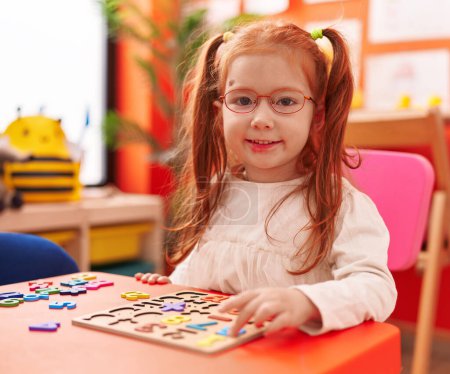 Photo for Adorable redhead girl playing with maths puzzle game sitting on table at kindergarten - Royalty Free Image