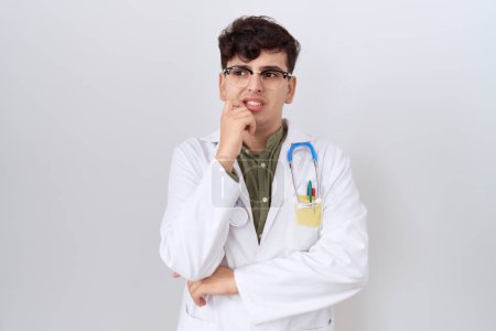 Téléchargez les photos : Young non binary man wearing doctor uniform and stethoscope looking stressed and nervous with hands on mouth biting nails. anxiety problem. - en image libre de droit