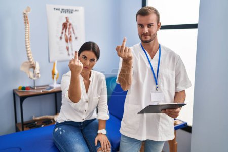 Foto de Young hispanic woman at physiotherapist appointment showing middle finger, impolite and rude fuck off expression - Imagen libre de derechos