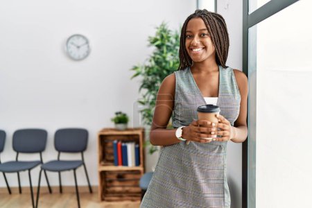 Téléchargez les photos : Jeune femme afro-américaine buvant du café debout dans la salle d'attente - en image libre de droit
