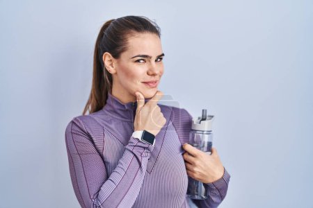 Photo for Beautiful woman wearing sportswear holding water bottle looking confident at the camera smiling with crossed arms and hand raised on chin. thinking positive. - Royalty Free Image