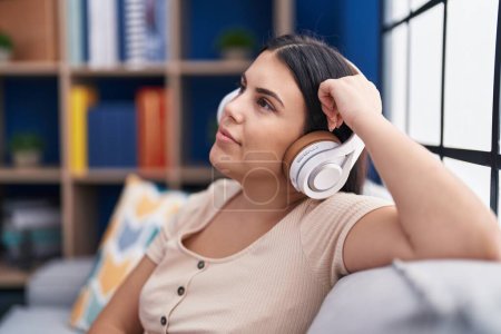 Téléchargez les photos : Jeune belle femme hispanique écoutant de la musique détendue sur le canapé à la maison - en image libre de droit