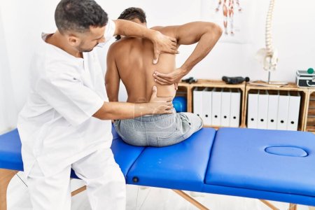 Photo for Two hispanic men physiotherapist and patient having rehab session massaging back at clinic - Royalty Free Image