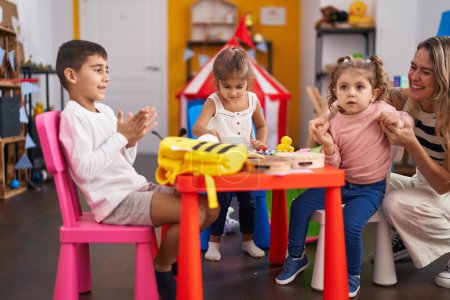 Foto de Maestro y grupo de niños sentados en la mesa aplaudiendo en el jardín de infantes - Imagen libre de derechos