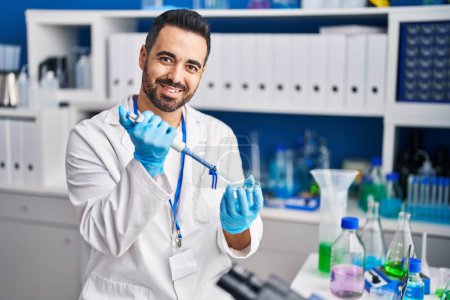 Téléchargez les photos : Jeune homme hispanique scientifique souriant confiant travailler au laboratoire - en image libre de droit