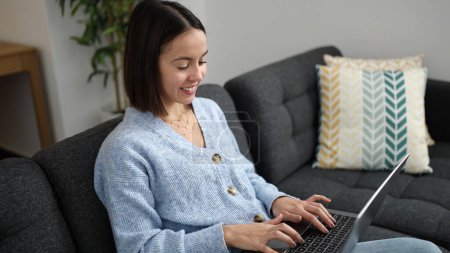 Photo for Young beautiful hispanic woman using laptop sitting on sofa at home - Royalty Free Image