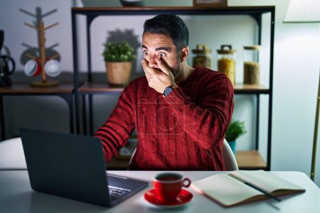 Photo for Young hispanic man with beard using computer laptop at night at home shocked covering mouth with hands for mistake. secret concept. - Royalty Free Image