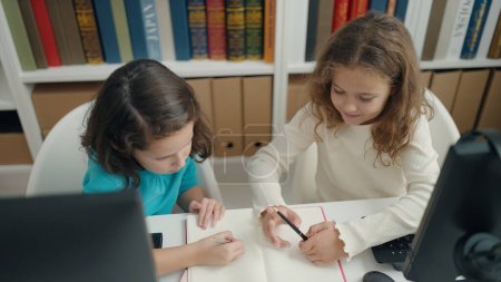 Téléchargez les photos : Two kids students using computer writing on notebook at classroom - en image libre de droit