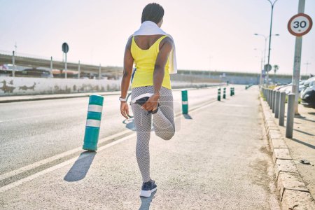 Foto de Mujer afroamericana usando ropa deportiva estiramiento pierna en la calle - Imagen libre de derechos