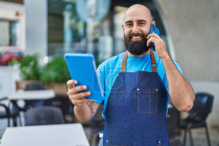 Téléchargez les photos : Jeune homme chauve serveuse touchpad smartphone à la terrasse du café - en image libre de droit