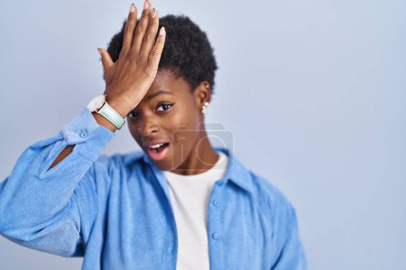 Foto de African american woman standing over blue background surprised with hand on head for mistake, remember error. forgot, bad memory concept. - Imagen libre de derechos