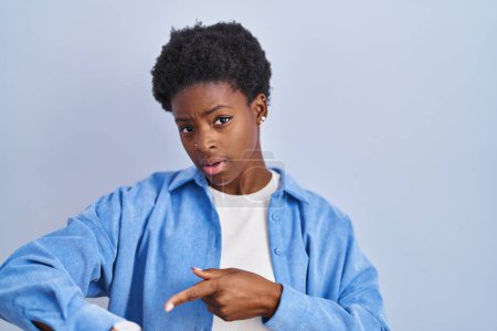 Téléchargez les photos : Femme afro-américaine debout sur fond bleu pressé pointant vers regarder le temps, l'impatience, bouleversé et en colère pour retard de délai - en image libre de droit