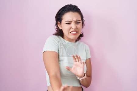 Foto de Mujer joven hispana de pie sobre fondo rosa expresión disgustada, disgustada y temerosa haciendo cara de disgusto porque reacción de aversión. - Imagen libre de derechos
