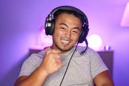 Photo for Chinese young man playing video games wearing headphones celebrating surprised and amazed for success with arms raised and eyes closed - Royalty Free Image