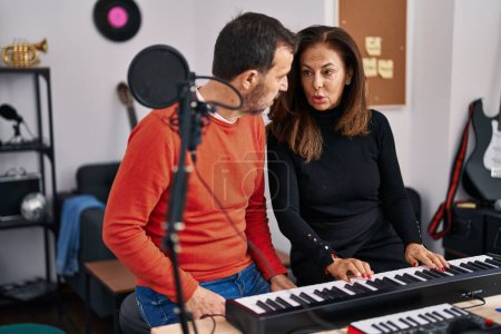Foto de Middle age man and woman musicians having keyboard piano class at music studio - Imagen libre de derechos