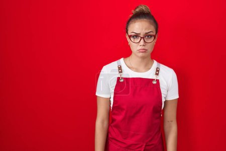 Photo for Young hispanic woman wearing waitress apron over red background skeptic and nervous, frowning upset because of problem. negative person. - Royalty Free Image