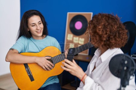 Téléchargez les photos : Deux femmes musiciens ayant une leçon de guitare classique par smartphone vidéo au studio de musique - en image libre de droit