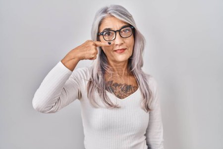 Téléchargez les photos : Middle age woman with grey hair standing over white background pointing with hand finger to face and nose, smiling cheerful. beauty concept - en image libre de droit