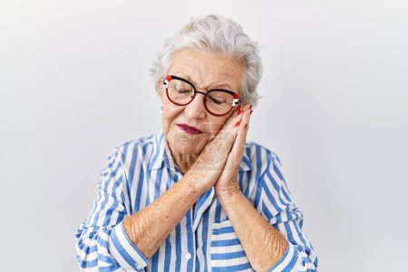Foto de Mujer mayor con el pelo gris de pie sobre fondo blanco durmiendo cansado soñando y posando con las manos juntas mientras sonríe con los ojos cerrados. - Imagen libre de derechos
