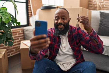 Foto de Joven afroamericano hombre hacer selfie por el teléfono inteligente con la llave de la nueva casa en el nuevo hogar - Imagen libre de derechos