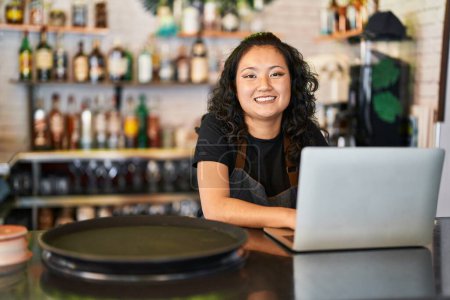 Foto de Joven camarera china sonriendo confiada usando laptop en restaurante - Imagen libre de derechos