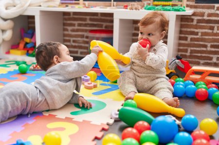 Téléchargez les photos : Deux adorables bébés jouant avec des boules et une quille assis sur le sol à la maternelle - en image libre de droit