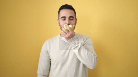 Téléchargez les photos : Jeune homme hispanique mangeant des pommes sur fond jaune isolé - en image libre de droit