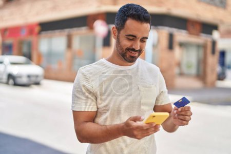 Téléchargez les photos : Jeune homme hispanique utilisant smartphone et carte de crédit à la rue - en image libre de droit