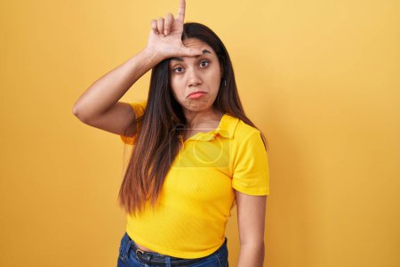 Téléchargez les photos : Young arab woman standing over yellow background making fun of people with fingers on forehead doing loser gesture mocking and insulting. - en image libre de droit