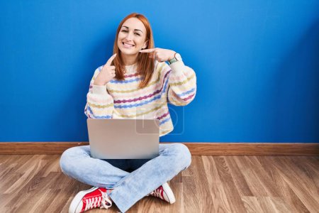 Téléchargez les photos : Jeune femme utilisant un ordinateur portable à la maison assis sur le sol souriant joyeuse montrant et pointant du doigt les dents et la bouche. concept de santé dentaire. - en image libre de droit
