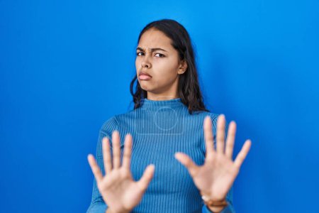 Photo for Young brazilian woman standing over blue isolated background moving away hands palms showing refusal and denial with afraid and disgusting expression. stop and forbidden. - Royalty Free Image