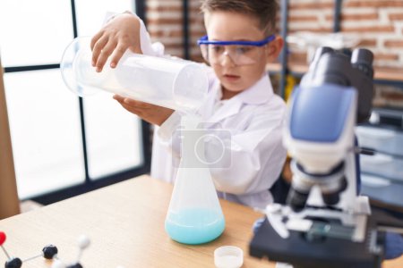 Foto de Adorable hispanic boy student pouring liquid on test tube at laboratory classroom - Imagen libre de derechos