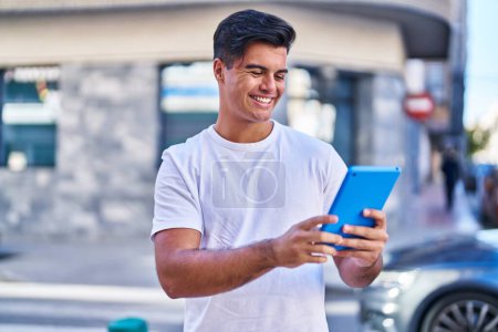 Foto de Young hispanic man smiling confident using touchpad at street - Imagen libre de derechos