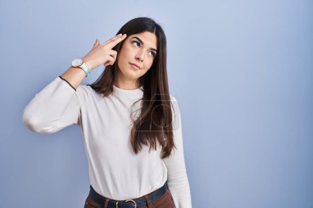 Téléchargez les photos : Young brunette woman standing over blue background shooting and killing oneself pointing hand and fingers to head like gun, suicide gesture. - en image libre de droit