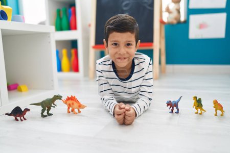 Foto de Adorable niño hispano jugando con juguetes de dino tirado en el suelo en el jardín de infantes - Imagen libre de derechos