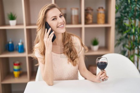 Photo for Young blonde woman talking on the smartphone drinking wine at home - Royalty Free Image