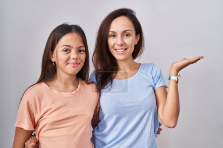 Téléchargez les photos : Jeune mère et fille debout sur fond blanc souriant gai présentation et pointant avec la paume de la main en regardant la caméra. - en image libre de droit