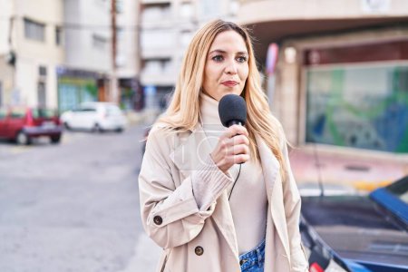 Téléchargez les photos : Jeune journaliste blonde travaillant au microphone dans la rue - en image libre de droit