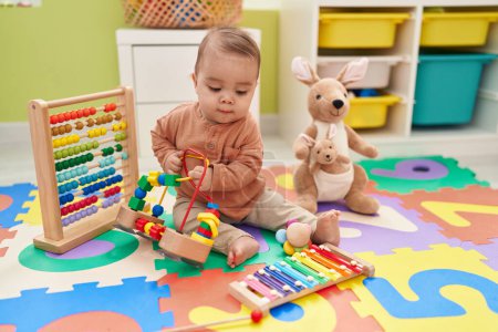 Foto de Adorable niño hispano jugando con juguetes sentados en el suelo en el jardín de infantes - Imagen libre de derechos